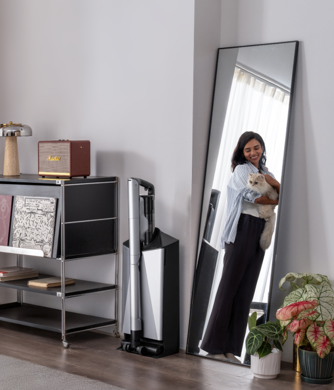 Narwal V50 Cube station beside shelving and a mirror reflecting a woman holding a cat